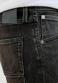Zbliżenie czarnych dżinsów z denimu pokazujących tylną kieszeń, szlufkę na pasek, metalowe nity oraz czarną metkę z nazwą marki Jack & Jones.