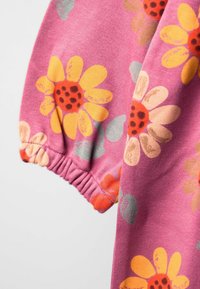 Lila Stoff mit großen gelben und orangefarbenen Blumen sowie schwarzen Zentren. Elastischer Bündchen-Detail an den Ärmeln. Weiche Textur.