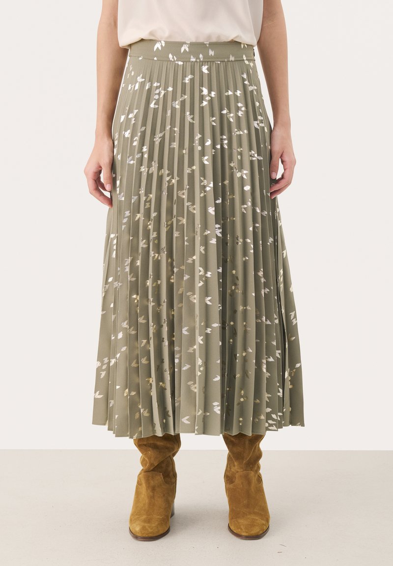 Plissé olijfgroene rok met zilveren loofdruk, gestructureerde stof en elastische tailleband, gecombineerd met lichtbruine suède enkellaarsjes.