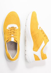 Yellow suede sneakers with white accents, perforated details, and thick white soles, shown from top and side views on a white background.