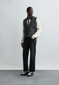 Sivi vuneni prsluk preko kremaste rebraste majice, uparen s tamnimfarmerkama i crnim cipelama s bijelim akcentima. Sadrži kopčanje na dugmad i džepove.