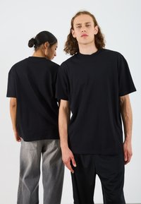 T-shirts en coton noir avec une coupe décontractée, col rond et manches courtes, portés par deux modèles faisant face à des directions opposées.