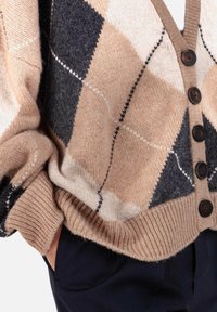 Cardigan beige et gris à motif losanges en laine douce, avec un profond col en V, de grands boutons marron, des poignets et un ourlet côtelés.