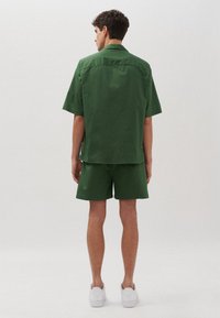 Camicetta verde a maniche corte e pantaloni abbinati realizzati in un tessuto leggero. Design semplice con una vestibilità comoda e dettagli hardware minimi.