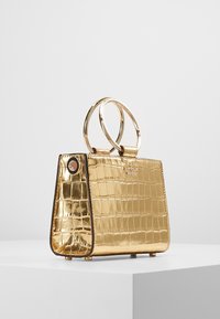 Borsa dorata con texture a effetto coccodrillo, manici metallici arrotondati e un piccolo logo dettagliato sul davanti, caratterizzata da una silhouette strutturata.