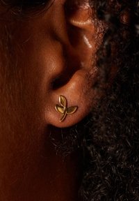 Gouden bladvormige studsierra op een close-up van een huidskleur, met een glad oppervlak en subtiele glans, met een veilige post achterkant.