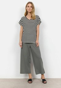 Sort og hvid stribet kortærmet top med v-hals, parret med løse grå brede bukser og sorte slidssandaler. Enkelt design.