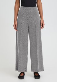 Bukser med vide ben i et sort-hvidt diagonalt stribet mønster, med høj talje og ben i lige snit. Materialet virker tekstureret og let.