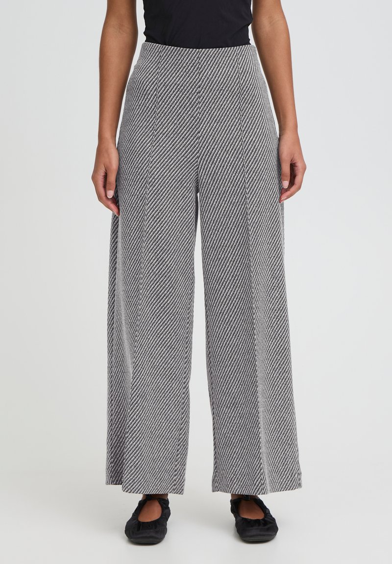 Bukser med vide ben i et sort-hvidt diagonalt stribet mønster, med høj talje og ben i lige snit. Materialet virker tekstureret og let.