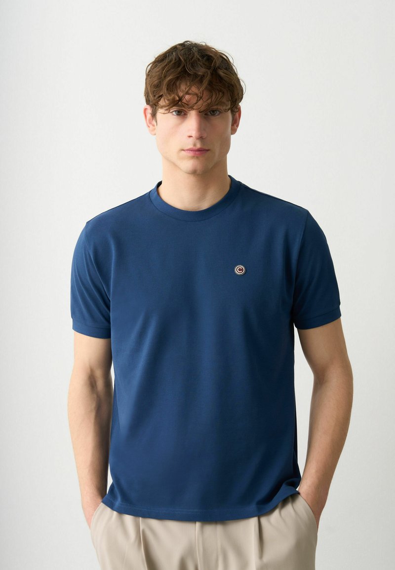 Mörkblå crew-neck t-shirt tillverkad av mjukt bomullstyg, med en liten cirkulär logotyp på bröstet och korta ärmar.