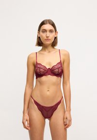 Ensemble de soutien-gorge et string en dentelle bordeaux avec de délicats motifs floraux, des bretelles ajustables et une texture de tissu semi-transparent.