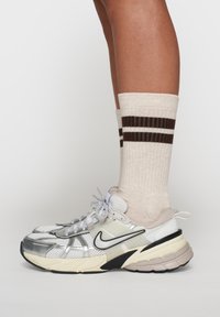 Scarpe da atletica argento e bianche con dettagli in rete e gomma, abbinate a calzini crema con strisce marroni.