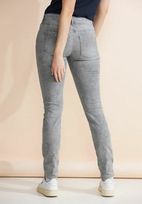 Harmaat slim-fit farkut, jossa on viisi taskua, sileä pinta, keskikorkea vyötärö ja hieno haalistuminen, yhdistettynä valkoisiin lenkkareihin.