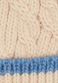 Knit beanie in cream wool with a textured cable pattern, featuring a textured blue stripe at the base. Soft and warm appearance.