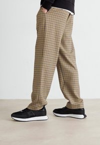 Brune og svarte rutete bukser med avslappet passform, med sidelommer og lett innsnevret ben, kombinert med svarte joggesko.