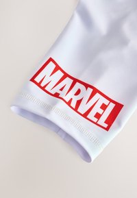 Manica atletica bianca con un prominente logo "MARVEL" rosso. Texture liscia con bordi cuciti e polsino aderente per una vestibilità sicura.