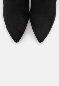 Los tacones de punta afilada de ante negro presentan un diseño elegante con una textura suave y sin hardware o acentos visibles.