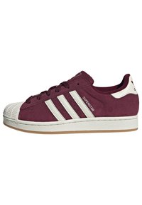 Maroon suede sneakers featuring a classic rubber shell toe, three white stripes on the side, and a gum sole. Accented with branding details.