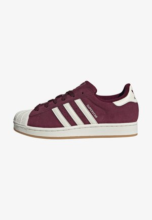 Bordeauxrote Wildleder-Sneaker mit einer klassischen Gummikappe, drei weißen Streifen an der Seite und einer Gummisohle. Mit Markenakzenten versehen.