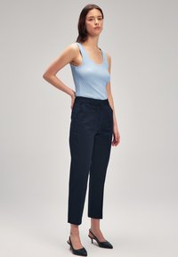 Canottiera a coste azzurro chiaro abbinata a pantaloni sartoriali blu navy, con un taglio elegante e gamba a sigaretta. Accessoriata con décolleté nere a punta.