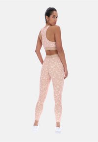 Femme de dos portant un soutien-gorge de sport et un legging imprimés léopard rose avec des tailles beige Ted Baker Sport et des baskets blanches.