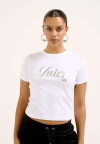 Biely cropped tričko vyrobené z bavlny, s kovovo strieborným logom "Juicy" v kurzíve. Krátke rukávy a okrúhly výstrih.
