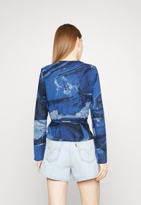 Top a maniche lunghe in tessuto blu con motivi astratti, caratterizzato da un design a vita stretta. Abbinato a pantaloni denim chiari, dà un aspetto casual.