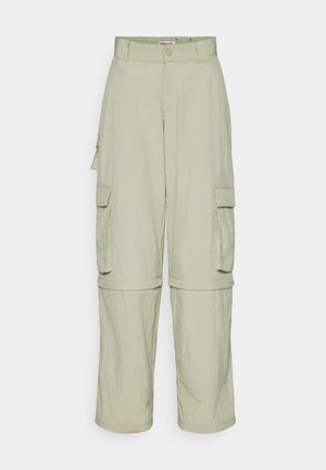 Pantalons cargo beiges clairs avec passants de ceinture, poches à rabat sur le côté et jambes zippées, se transformant en shorts.