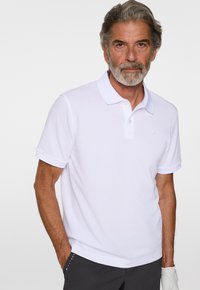 Vit polo-shirt med klassisk krage, korta ärmar, subtil logotyp på bröstet och ett mjukt, andningsbart material.