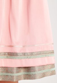 Jupe en tissu rose clair avec des bandes brodées de fleurs argentées et un galon de pompons verts près de l'ourlet.