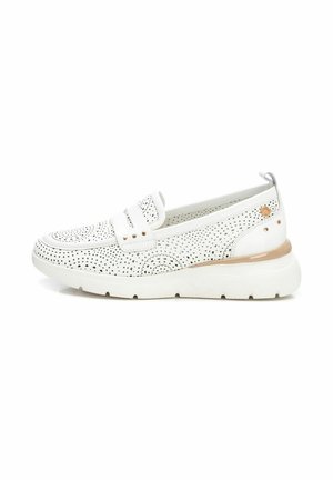 Zapatos blancos sin cordones con diseño perforado, pequeños puntos negros en contraste, suela blanca gruesa y un sutil acento beige cerca del talón.