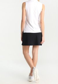 Bílý top bez rukávů s vysokým límcem, doplněný černou sukní. Nosené s bílými sportovními botami. Hladká látka, jednoduchý design, minimální detaily.