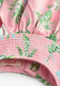 Růžové květinové šaty s zelenými listovými vzory, elastickým nařaseným pasem a štítkem označeným "Cat Kid London." Hladká bavlněná látka.