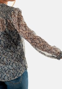 Blusa transparente con un patrón texturizado en tonos de azul y marrón. Mangas largas, escote fruncido y dobladillo ligeramente curvado.