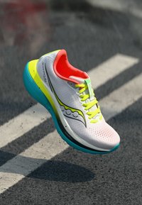 Zapatilla de running con una parte superior de malla blanca transpirable, brillantes acentos neón en rosa y verde, y una suela acolchada turquesa con un diseño elegante.