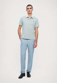 Polo de culoare albastru deschis cu mânecă scurtă și un model subtil, asortat cu pantaloni dungi în dungi albastre deschise și pantofi negri. Detaliu alb la guler vizibil.