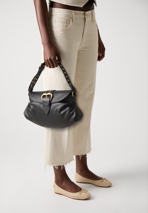Zwart leren handtas met een gouden gesp, gecombineerd met crèmekleurige broeken met wijde pijpen en franjes aan de onderkant, en beige ballerina's.