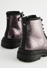 Stivaletti ankle metallici viola con suola in gomma nera, dettaglio con zip e accent hardware a forma di stella. Finitura testurizzata e caviglia imbottita per il comfort.