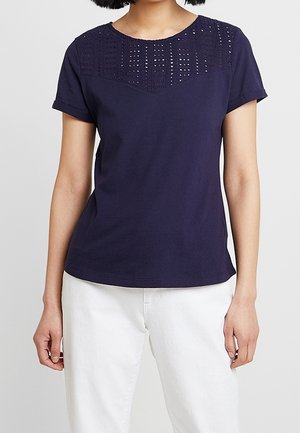 Marineblå t-shirt med korte ærmer og dekorativt øjeslyngemønster på bærestykket, lavet af blød bomuld, med rund halsudskæring og afslappet pasform.