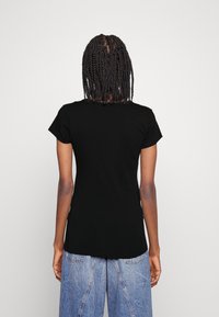 Zwarte t-shirt met korte mouwen, ronde halslijn en een getailleerde stijl, gezien vanaf de achterkant, gecombineerd met lichtblauwe denimjeans.