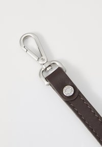 Bruine leren band met een zilveren metalen sluiting. Bevat een decoratieve zilveren knop met gegraveerde tekst en een gestikte patroon langs de rand.