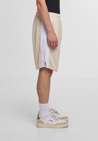 Beige Sportshorts mit weißen Seitenpanelen, aus leichtem Material. Sie verfügen über einen elastischen Bund und seitliche Schlitze für optimale Bewegungsfreiheit.