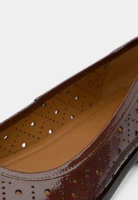Μπαλαρίνα από δέρμα μπορντό με διάτρητο σχέδιο, λεία υφή, στρογγυλεμένη μύτη και αντίθετη μπεζ εσωτερική επένδυση.