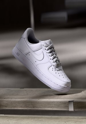 White Nike Air Force 1 sneaker with laces floating above a concrete bench against a dark, blurred background.