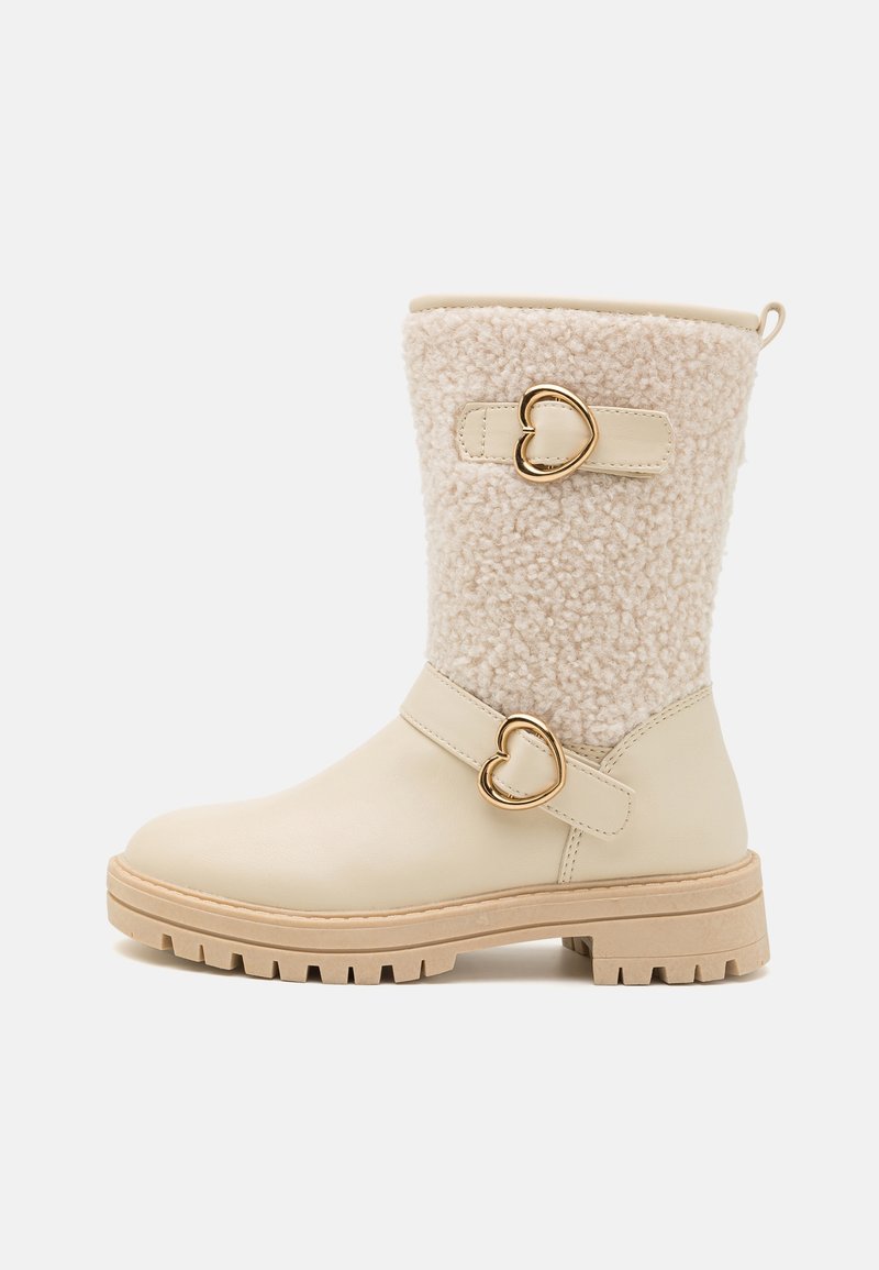 Botte couleur crème mi-mollet avec dessus en shearling, deux boucles dorées en forme de cœur et une semelle beige robuste.