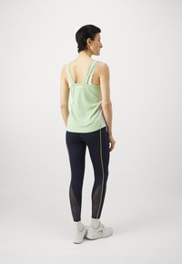 Lichtgroene sporttanktop met racerback-ontwerp, gecombineerd met marineblauwe leggings met meshpanelen en lichtgroene zijstrepen.