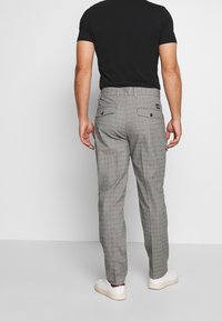 Pantalones a cuadros grises con corte Slim Fit, que cuentan con bolsillos traseros y pasadores para cinturón, combinados con una camiseta de manga corta negra y zapatos blancos.