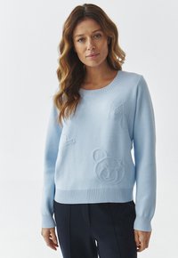 Pull léger bleu en tissu doux avec des poignets et un ourlet côtelés. Présente des motifs en relief subtils d'un ours et de nuages.