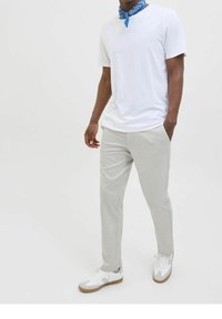 Bílá tričko, světle šedé kalhoty a bílé tenisky s jemnými šedými akcenty. Také má kolem krku modrou bandanu.