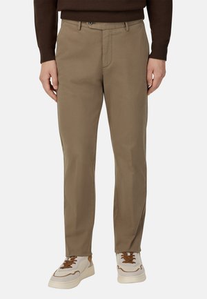 Khaki-Hosen mit geradem Schnitt, aus glattem Material. Mit Reißverschluss, Gürtelschlaufen und Seitentaschen. Getragen mit weißen Sneakern.